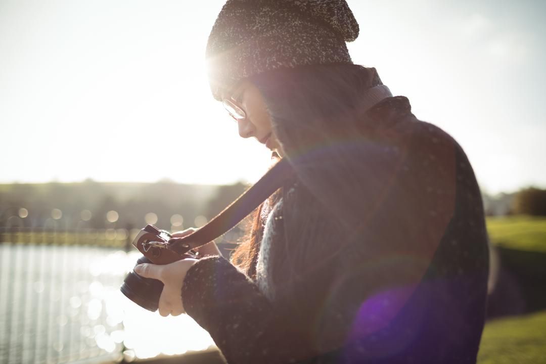 Mujer mirando su cámara junto a un lago - Qué incluir en tus vídeos Detrás de escena en YouTube - Imagen