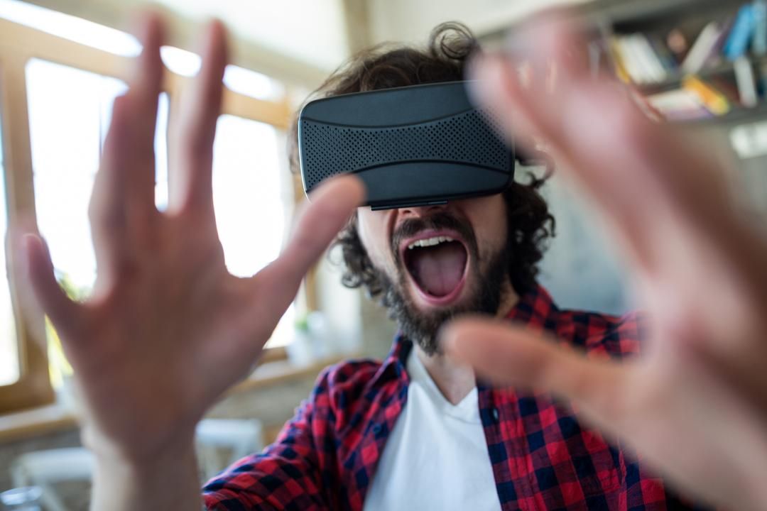 Homem entusiasmado com uma camisa xadrez vermelha e fone de ouvido VR aponta as mãos para a câmera - O que são canais de jogos no YouTube - Imagem