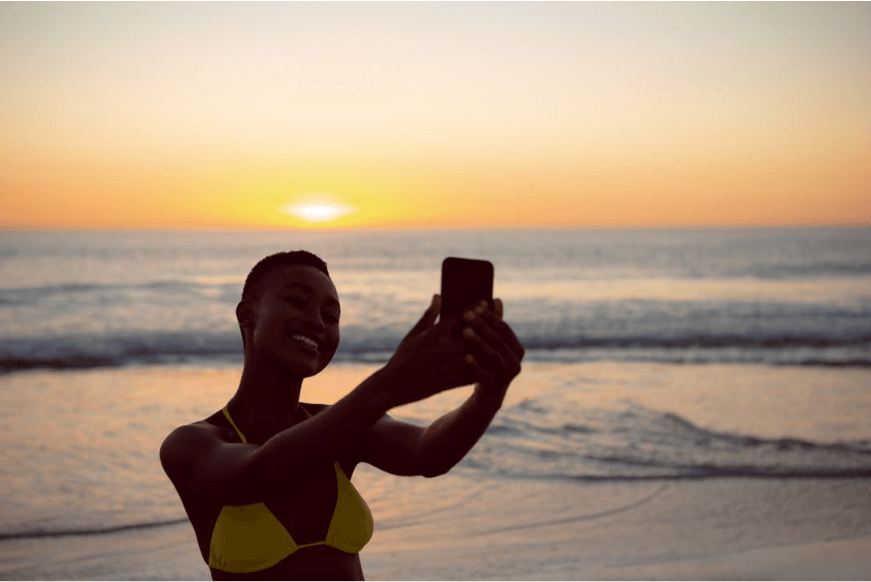 Mulher de biquíni tirando selfie com o celular na praia - Top 10 vloggers de viagens do YouTube - Imagem