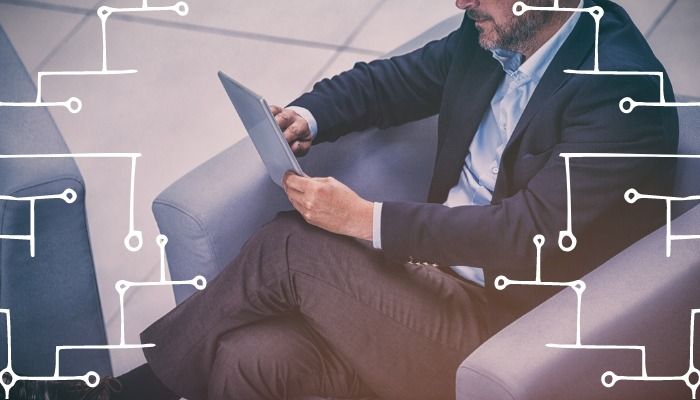 Un hombre sentado en una silla y trabajando en su tableta con un símbolo de red blanco rodeando la imagen - Adapte su estrategia y contenido para adaptarse a los recorridos y puntos de contacto del cliente - Imagen