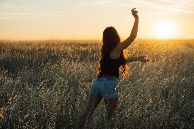 A girl in shorts in a field stretches her hands towards the sun - Bright and moody colour palettes continue to dominate in 2019 - Image
