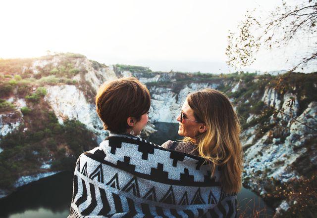 Vue arrière de deux jeunes femmes enveloppées dans une couverture regardant les montagnes - Les photos de bureau mises en scène pourraient bientôt appartenir au passé - Image