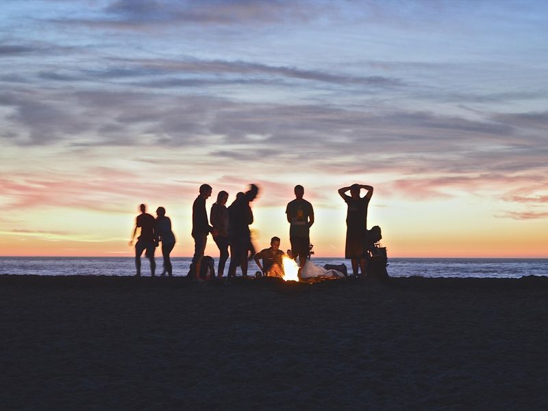 Freunde hängen am Strand am Lagerfeuer ab – Vorteile einer Geburtstagsfeier im Freien – Bild