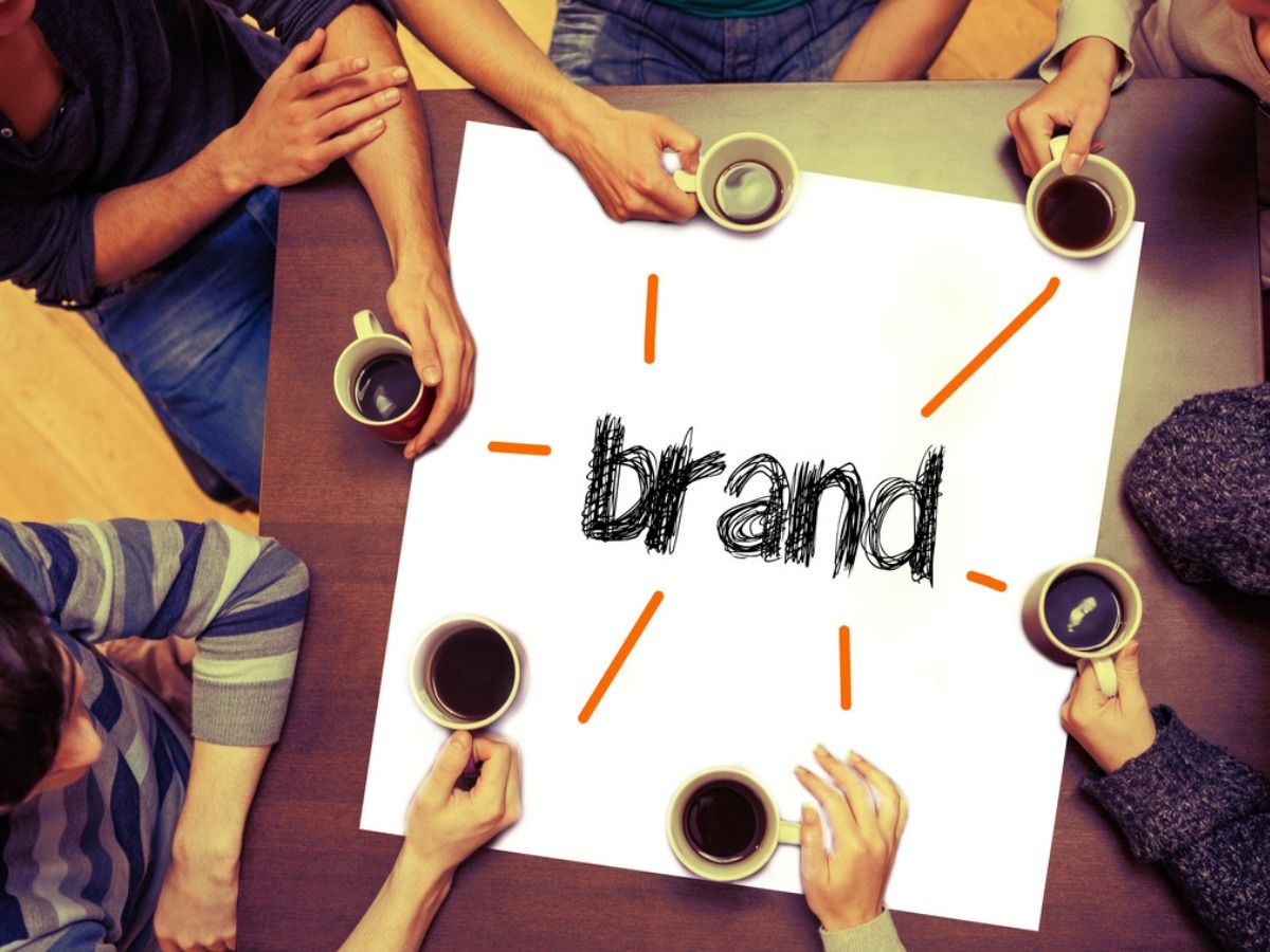 People with cups of coffee look at a piece of paper with a handwritten title 'Brand' - Boosting brand awareness with sponsered events - Image