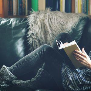 Person reading a book on a leather couch with a bookcase in the background - Reliable creative marketing strategies for your business that actually work - Image