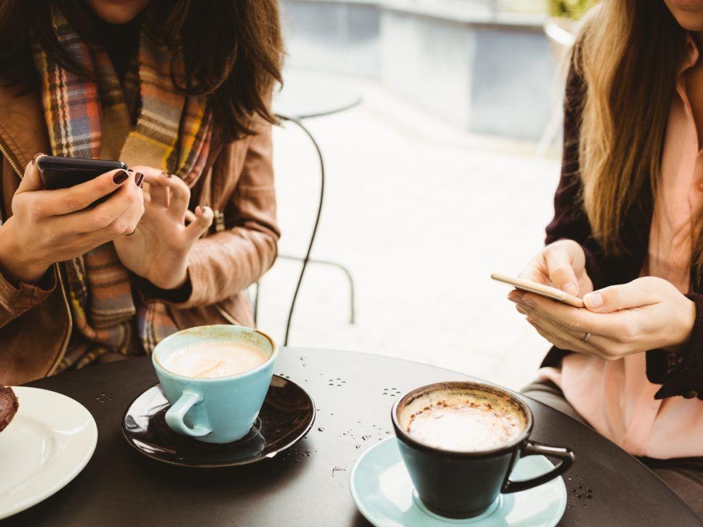 Deux femmes en train de texter sur leurs téléphones pendant qu'elles prennent un café - Stratégies de marketing créatives et fiables pour votre entreprise qui fonctionnent réellement - Image