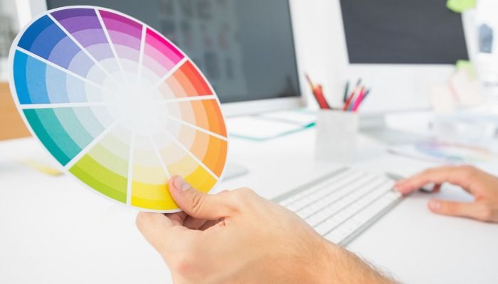 An employee works with the computer, holding a color wheel in hand - Creative Marketing Ideas and Strategies - Image