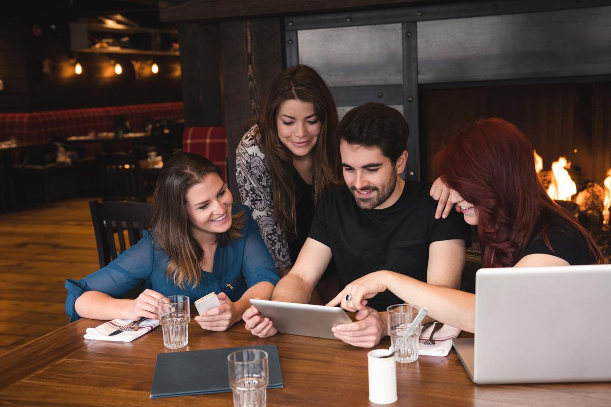 Eine Gruppe von vier Personen in einem Restaurant schaut sich etwas auf einem Tablet an - Ein umfassender Leitfaden, wie man mehr Aufrufe auf YouTube bekommt - Bild