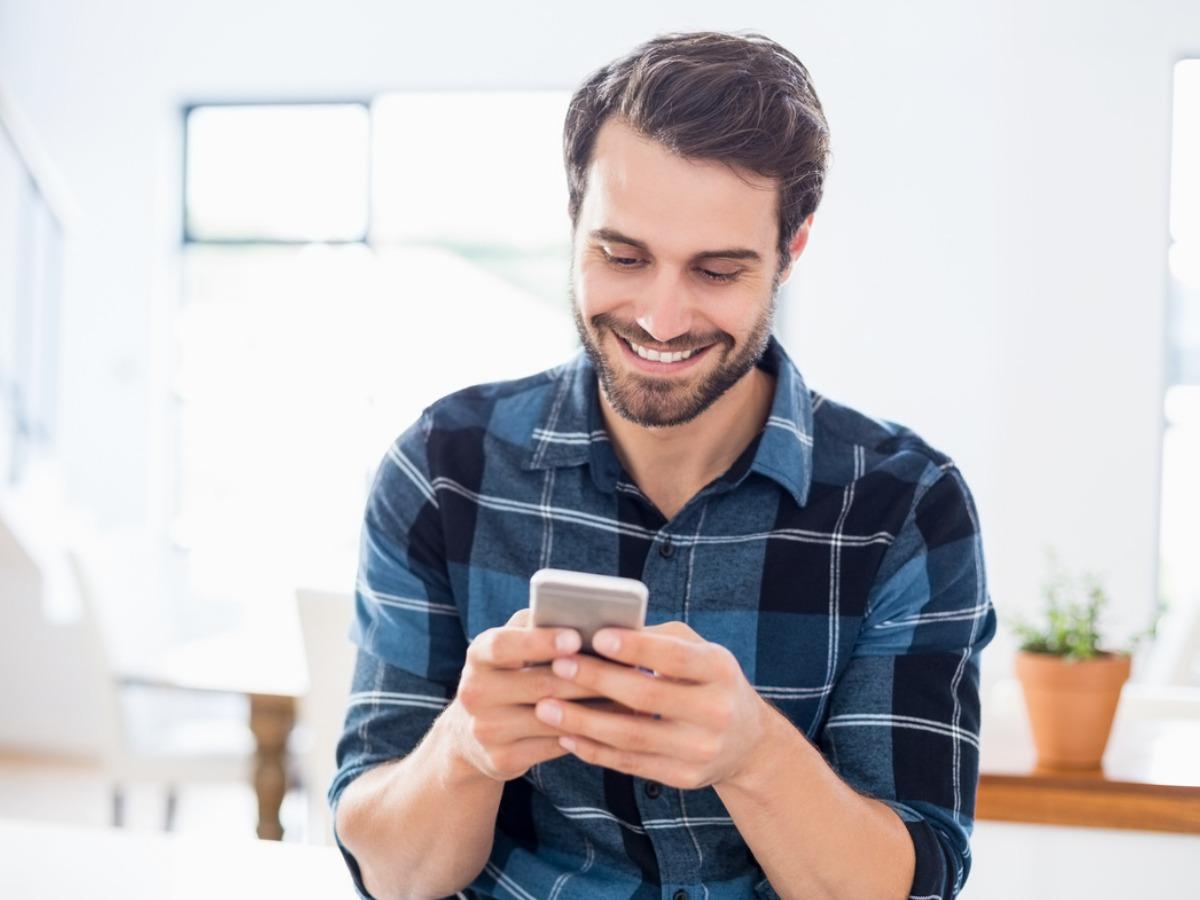 A smiling man in a shirt is scrolling through his phone - Step-by-step guide to designing YouTube thumbnails - Image