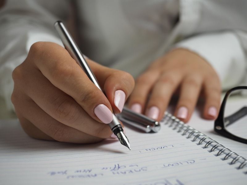 Frau mit lackierten Nägeln schreibt in ein Notizbuch