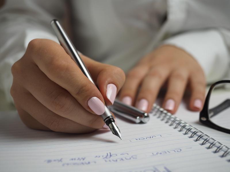 Woman with painted nails writing in a notebook - How to start a vlog: Everything you need to know - Image