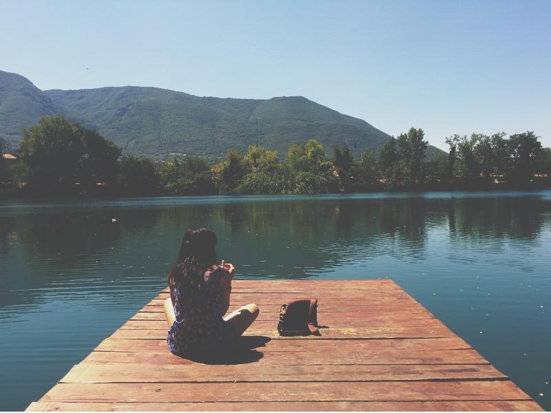 mujer sentada en una repisa de madera mirando el río y un hermoso paisaje