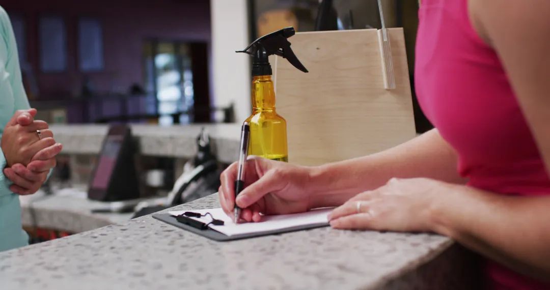 Midsection of caucasian woman filling in forms on counter at reception of gym - Image