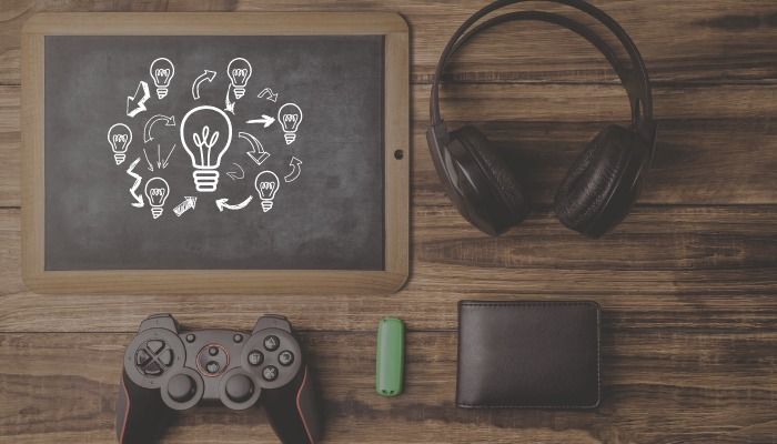 A chalkboard, wireless headphones, gamepad, wallet, and thumb drive lie on a wooden table - Learn the top 15 marketing trends to improve your business and marketing strategy - Image