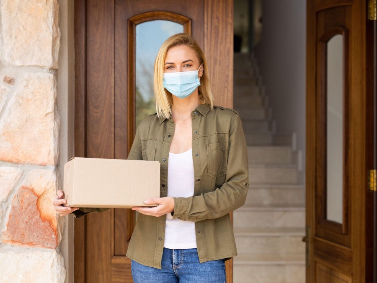 Woman wearing a mask standing outside the front door of her house while holding a package20 proven real estate marketing ideas to help attract qualified buyers - Image
