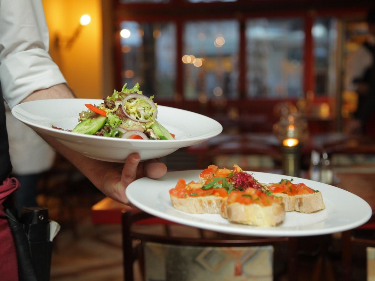 Waiter holding two plates of food at restaurant - Restaurant marketing ideas: how to attract new customers to your restaurant - Image