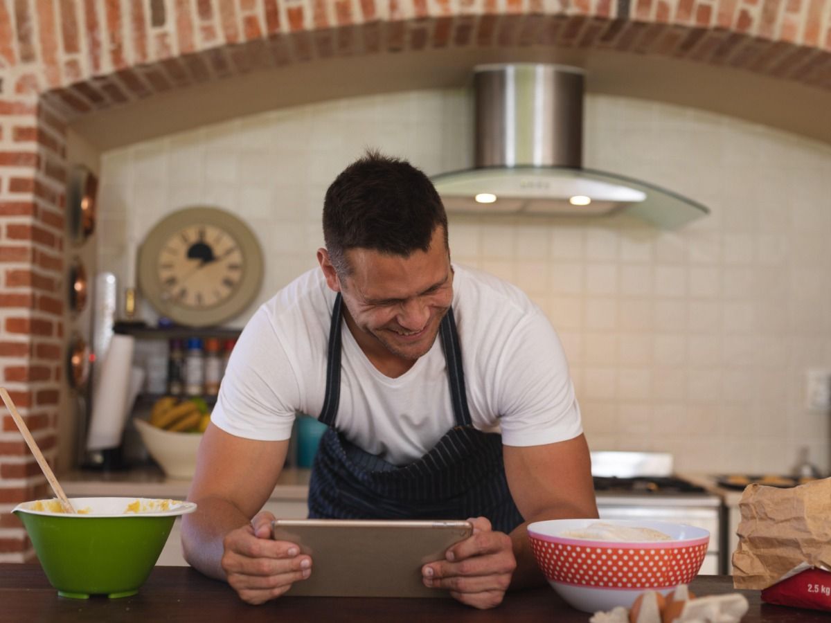 Hombre en una tableta en la cocina con platos
