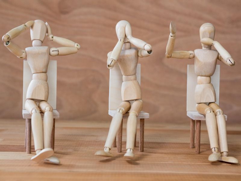Three figurine, representing the mute, deaf and blind senses, sit on chairs on a wooden background - How to make a resume that stands out - Image