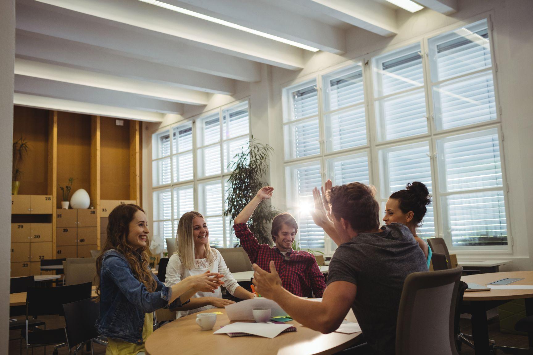 Équipe à table souriante et high fiving - idées de stratégie de vente - image