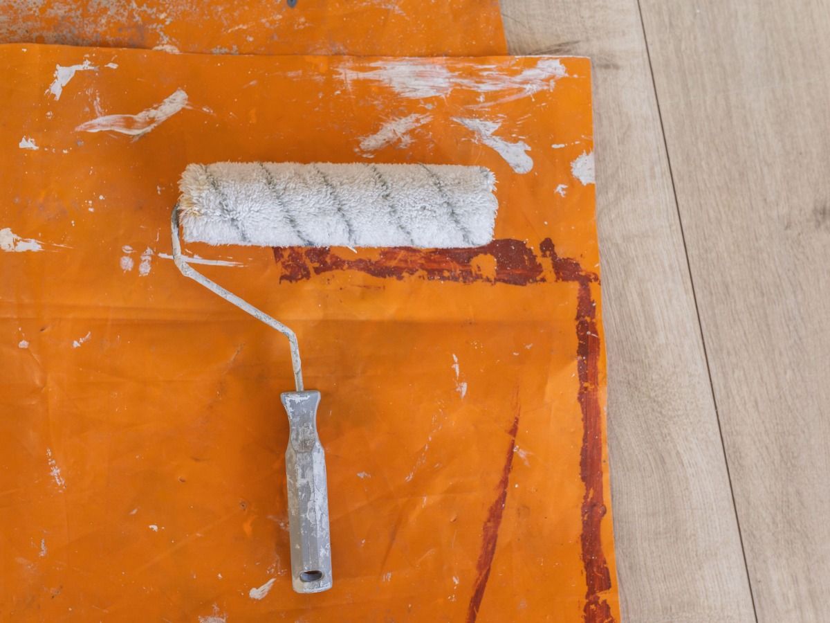 Rolo de pintura na tampa de plástico laranja no piso de madeira