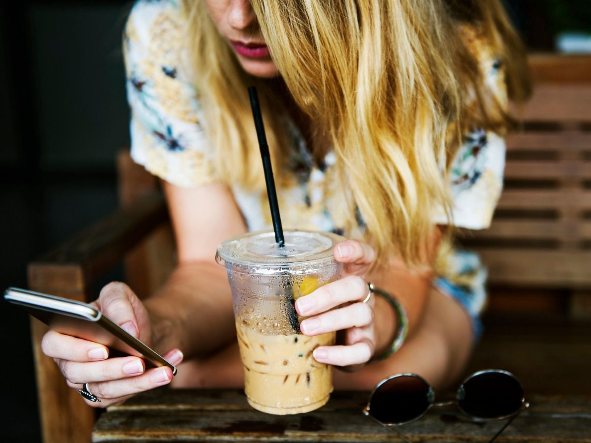 Mulher loira bebendo café gelado e usando smartphone