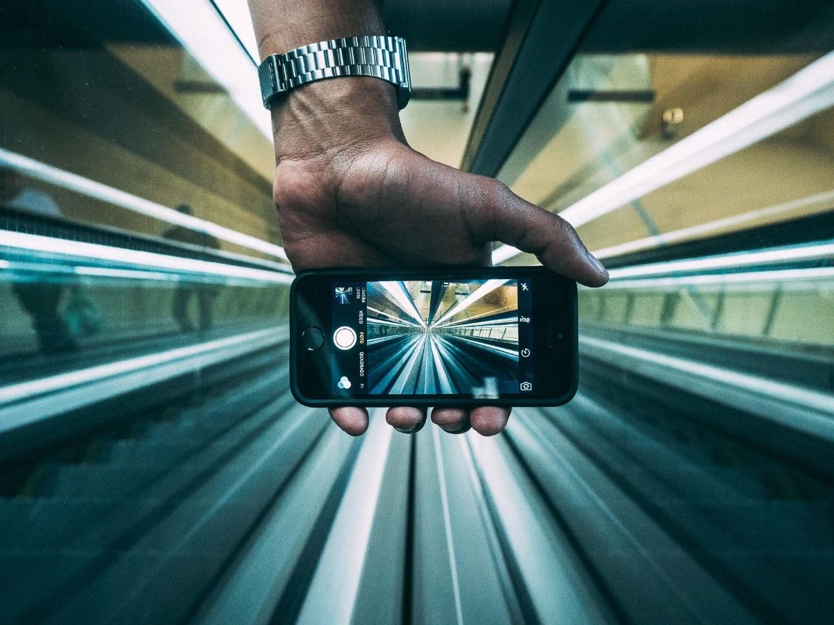 Hand holding smartphone camera to film escalator - The ultimate guide to social media marketing for beginners - Image