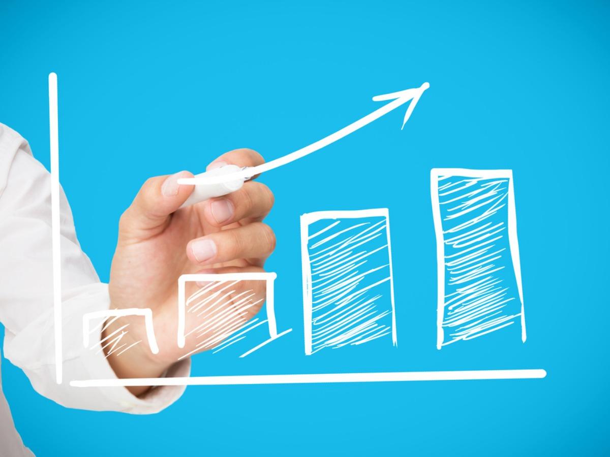 Bar chart with rising arrow, over a blue background with a person drawing it - Tips for creating a social media content calendar: Key factors to consider - Image