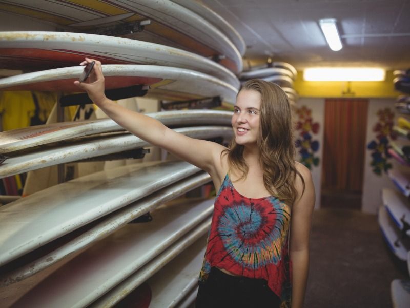 A young woman takes a selfie in a surfboard shop - The best social media marketing tips for starting and growing your business - Image
