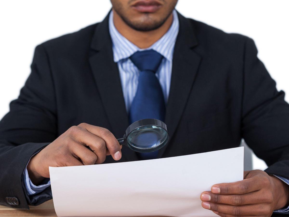 A male businessman in a suit checks documents with a magnifying glass - The ultimate brand audit guide - Image