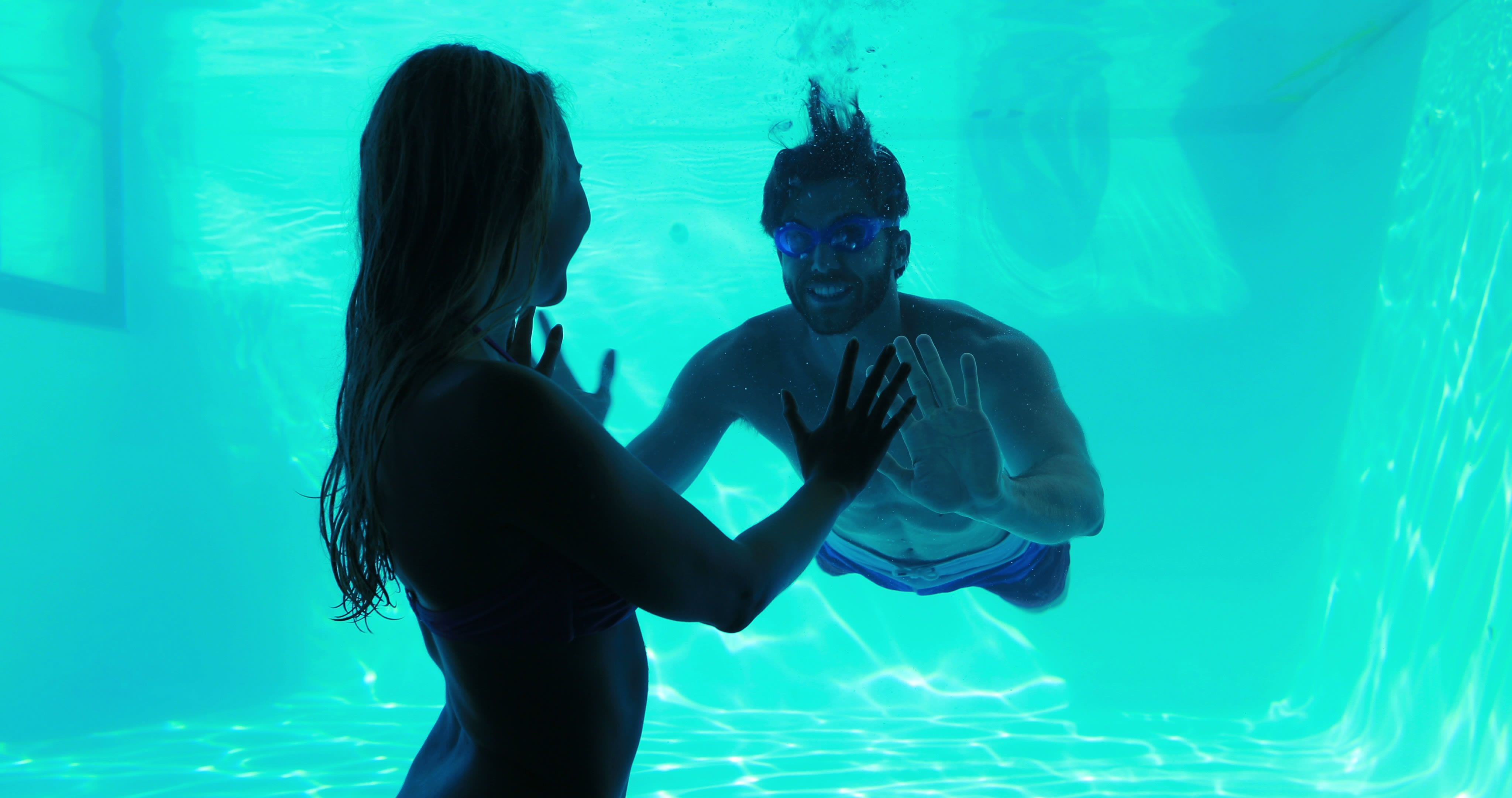 Amis profitant de la natation sous-marine dans une piscine avec éclairage bleu - Image