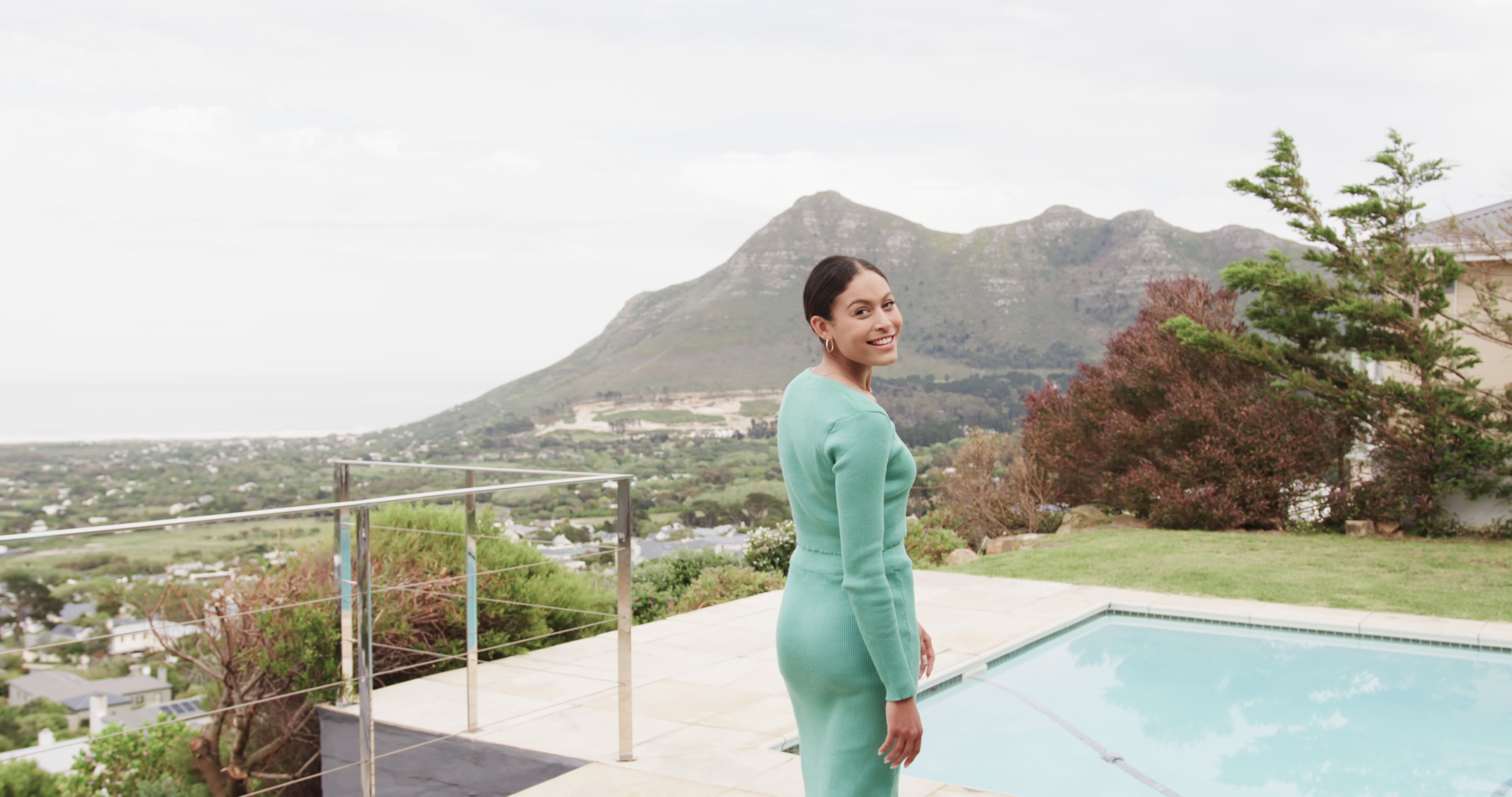 Mujer elegante en vestido turquesa junto a piscina lujosa con vista a la montaña imagen