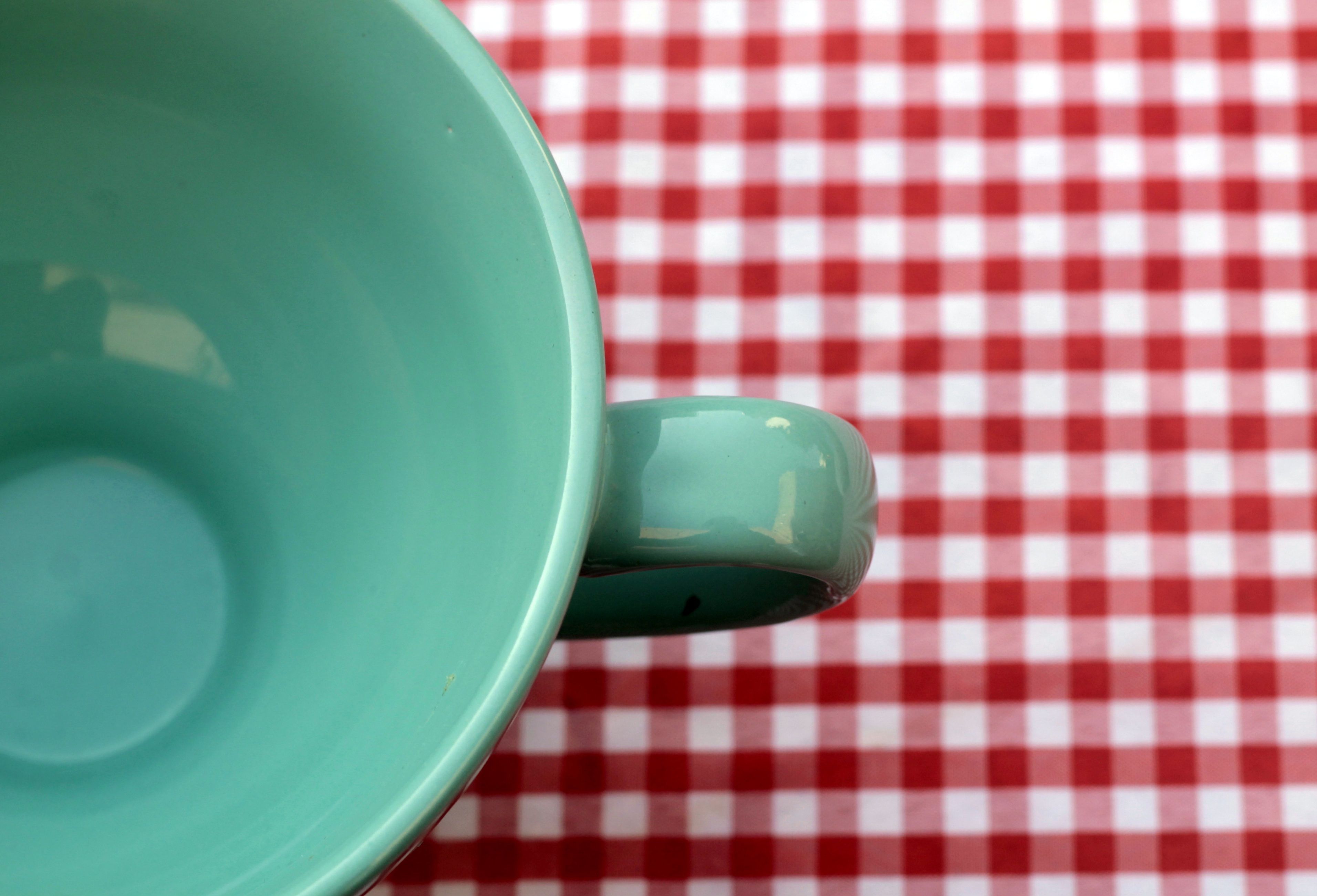 Taza de café turquesa vacía sobre mantel de cuadros rojos y blancos - Imagen