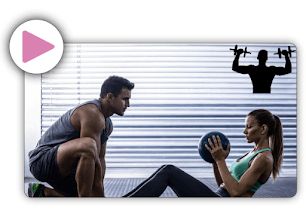 Una mujer en el gimnasio con una pelota en sus manos apoyada por un entrenador